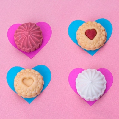 Quatro bolachas decorativas com padrões e corações sobre corações de papel em fundo rosa.