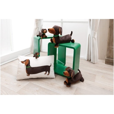 Peluches de cachorro salsicha castanho com coleira verde sobre bancos verdes e almofada branca com estampa do cachorro