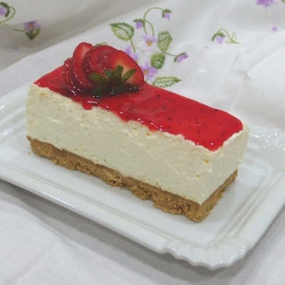 Fatia de cheesecake com cobertura vermelha e morangos num prato branco