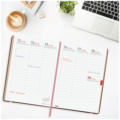Planificador semanal aberto com anotações, chávena de café latte, planta, caneta e teclado num fundo branco
