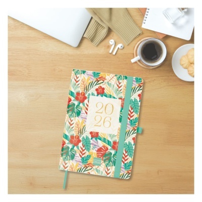 Agenda floral 2026 com elástico verde sobre mesa com café, bolachas, headphones, caderno e computador
