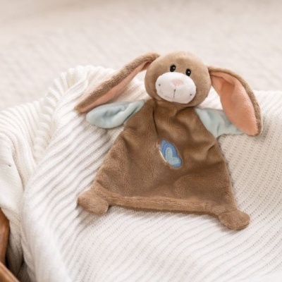 Peluche castanho de coelho com padrão de borboleta azul numa manta branca