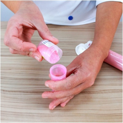 Mãos a abrir frasco plástico rosa com pastilhas rosa sobre superfície de madeira