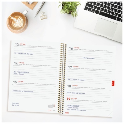 Agenda aberta com anotações, café, planta, clips, caneta e teclado de portátil num fundo branco