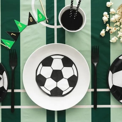 Mesa de festa com tema de futebol com pratos, guardanapos, copos e decoração em preto, branco e verde.