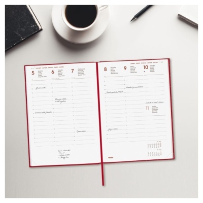 Agenda semanal aberta com capa vermelha e caneca de café numa mesa branca