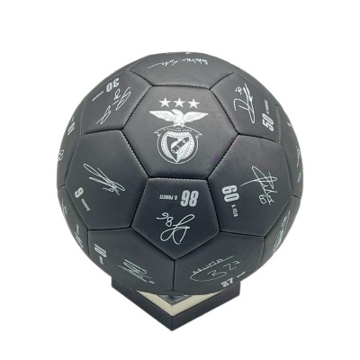 Bola de futebol preta com escudo do SLB e assinaturas brancas num suporte preto