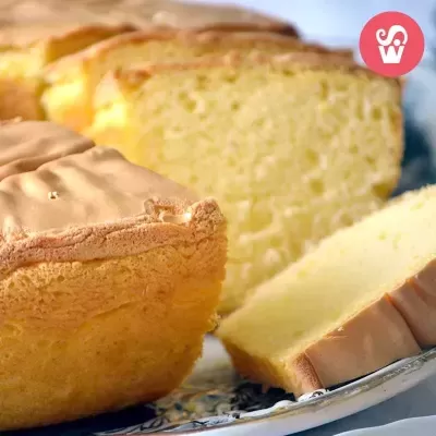 Bolo fofo amarelo cortado em fatias num prato branco com borda azul