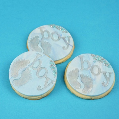 Três bolachas decoradas com pegadas prateadas e a palavra boy em fundo azul e branco