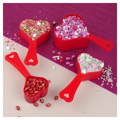 Medidores vermelhos em forma de coração com confeitos coloridos, fundo rosa brilhante e bege