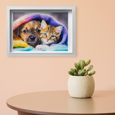 Quadro com imagem de cão e gato debaixo de cobertor colorido, pendurado em parede peach acima de mesa com planta suculenta.