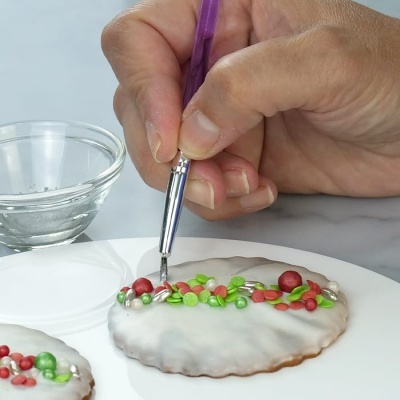 Mão a decorar bolacha com glacé e enfeites coloridos com pincel roxo