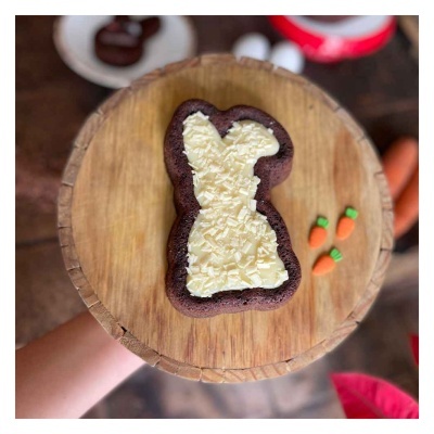 Bolo em forma de coelho com cobertura branca e granulados, base de madeira e miniaturas de cenouras