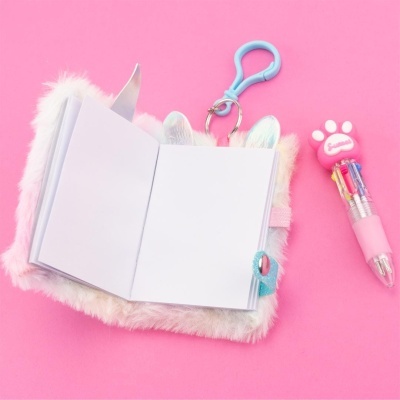 Caderno felpudo branco com orelhas e caneta rosa com ponta de pata em fundo rosa.
