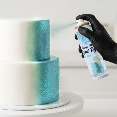 Bolo branco de dois andares com pintura azul Tiffany aplicada com spray metalizado por uma mão com luva preta