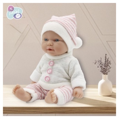 Boneca de bebé com roupa rosa e branca sentada numa superfície de madeira junto a um vaso branco com planta seca