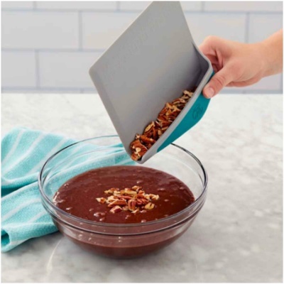 Mão a despejar nozes numa taça de vidro com mistura de chocolate.