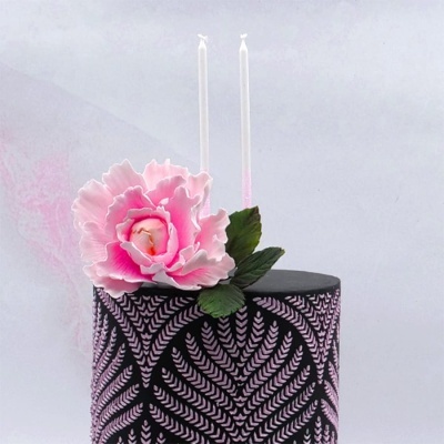 Bolo decorado preto com padrão rosa, flor grande rosa e duas velas.