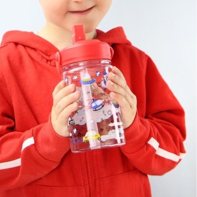 Copo infantil transparente com tampa e desenhos coloridos, segurado por criança de casaco vermelho