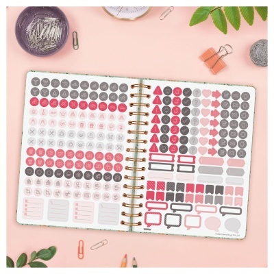 Agenda aberta com autocolantes coloridos e vários clips ao redor sobre fundo rosa