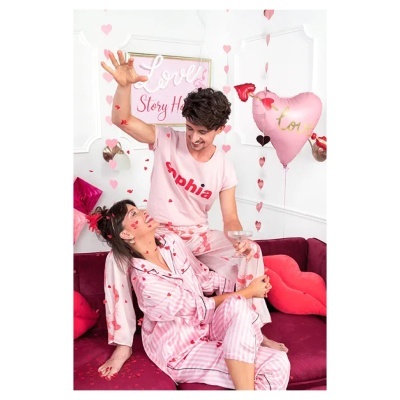 Casal de pijamas rosas com decoração de amor em sofá roxo