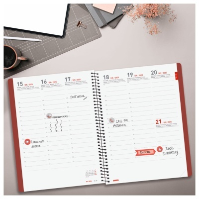 Planner semanal aberto com capa vermelha, notas manuscritas e objetos de secretária