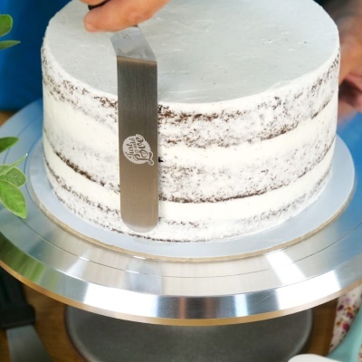 Bolo redondo com camada fina de creme branco e espátula metálica a alisar o bolo