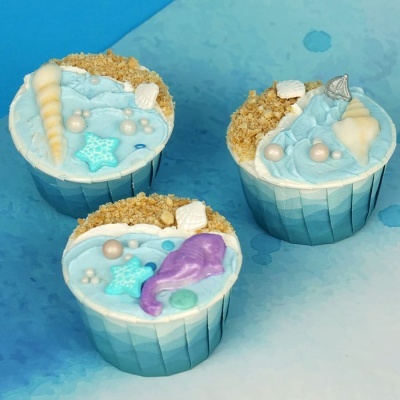 Três cupcakes decorados com tema marinho, conchas e estrelas do mar, em forminhas azuis