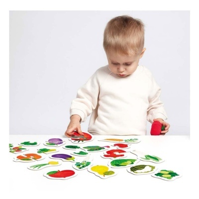 Criança a brincar com cartas ilustradas de frutas e vegetais sobre mesa branca