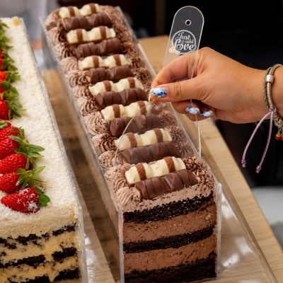 Fatia de bolo de chocolate com creme, chocolate e embalagem transparente.
