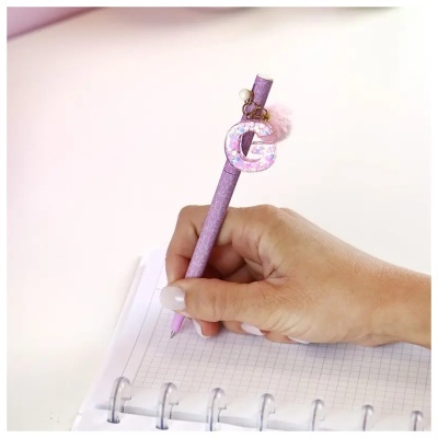 Caneta lilás com pendente da letra G a escrever em caderno quadriculado