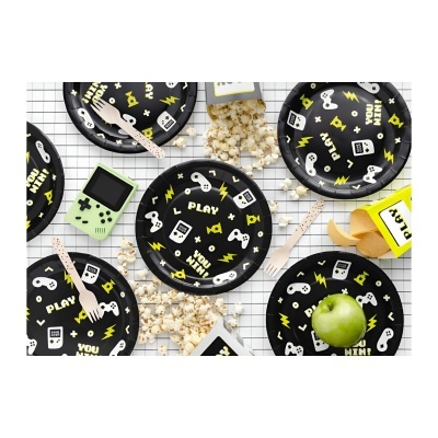 Pratos pretos com desenhos de videojogos e texto, maçã verde, pipocas e aparelho gameboy sobre fundo xadrez branco