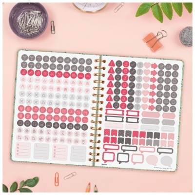 Caderno com adesivos coloridos e objetos de escritório sobre superfície rosa