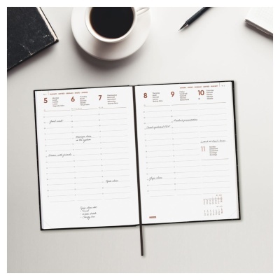 Agenda aberta numa mesa com chávena de café, caderno e uma caneta