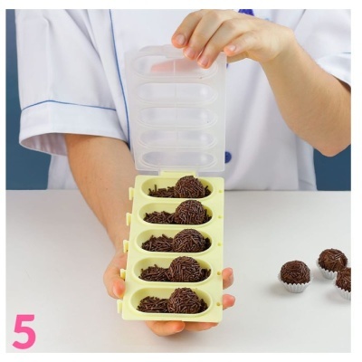 Forma de silicone amarela com brigadeiros mole na mão de pessoa com bata branca sobre mesa branca