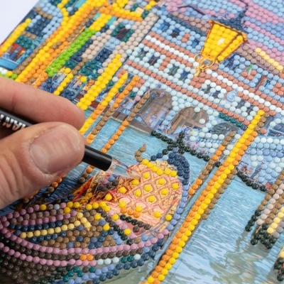 Mão aplicando diamantes numa pintura com imagem de gôndola colorida