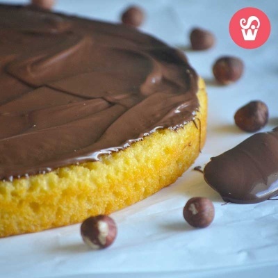Bolo de chocolate com avelãs e barra de chocolate numa superfície branca