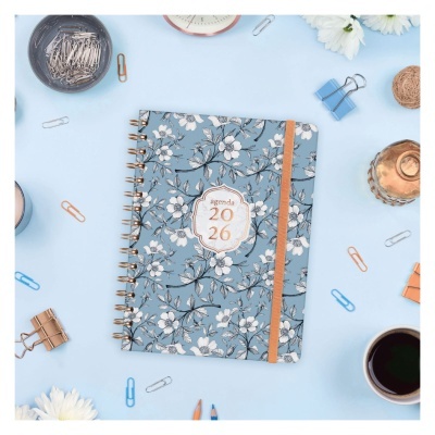 Caderno agenda 2026 com capa azul e flores brancas num ambiente de escritório com acessórios