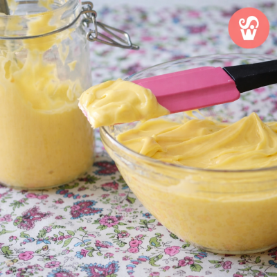 Bacia e frasco de vidro com creme amarelo e espátula rosa sobre toalha floral.