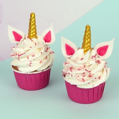 Dois cupcakes decorados como unicórnios com cobertura branca, granulados rosa e cornos dourados