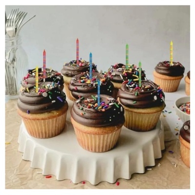 Cupcakes com creme de chocolate e velas coloridas em suporte branco.