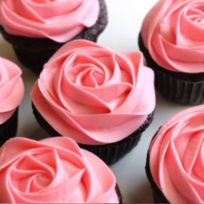 Seis cupcakes de chocolate com cobertura rosa em espiral tipo rosa sobre superfície branca
