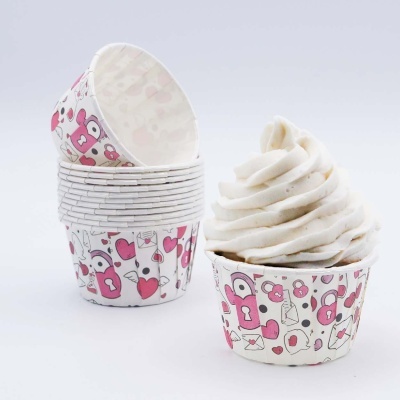 Formas de papel para cupcake com padrão de corações e chave rosa e branco, com cupcake e cobertura branca ao lado