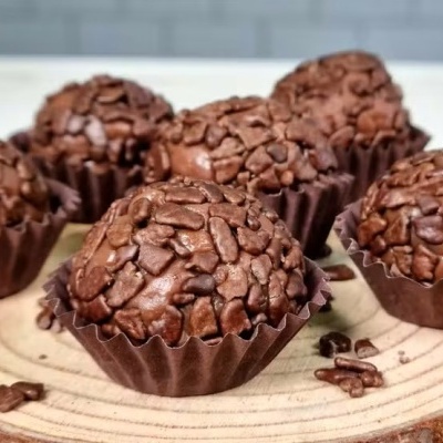 Brigadeiros de chocolate com granulado em forminhas sobre tábua de madeira
