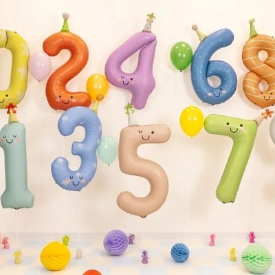 Balões de números coloridos com rostos sorridentes e chapéus, e balões pequenos em ambiente interior