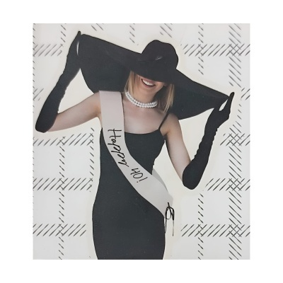 Mulher com vestido preto, luvas compridas e chapéu grande preto com faixa branca 'Happy 40!'.