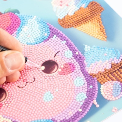 Quadro de diamantes com padrão de gato rosa e cone de gelado em fundo azul com aplicação de pequenos cristais coloridos.