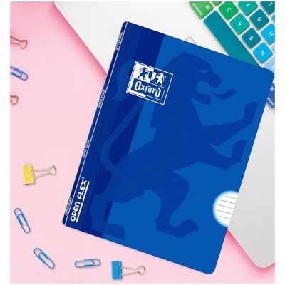 Caderno azul Oxford Open Flex com desenho de leão, teclado colorido e clipes de papel numa mesa.