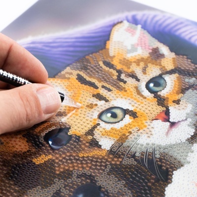 Mão usando ferramenta para aplicar pedras coloridas formando figura de gato em mosaico