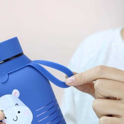 Garrafa de água azul com ilustração de urso e alça flexível segurada por mão.